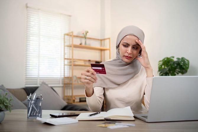 イスラム教徒の女性がパソコンの前でクレジットカードを見て悩んでいる