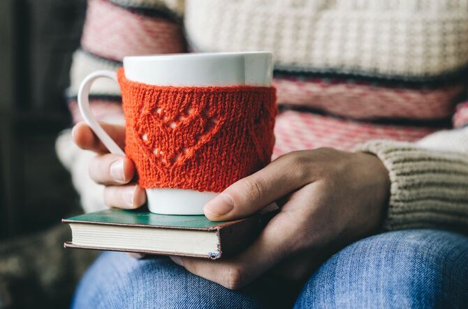 女性の手とホットドリンクの本とカップ