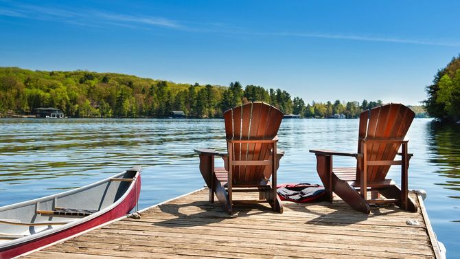 湖のウッドデッキにデッキチェアが2脚、左手に舟
