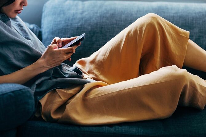 スマートフォンを使いながらソファでくつろぐ若い女性