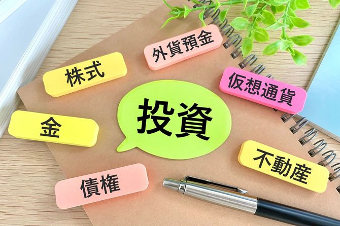 ノートの上に置かれた吹き出し型の付箋には「投資」他の付箋も、株式、金、債券、外貨預金、仮想通貨、不動産と投資に関係のある言葉が並ぶ