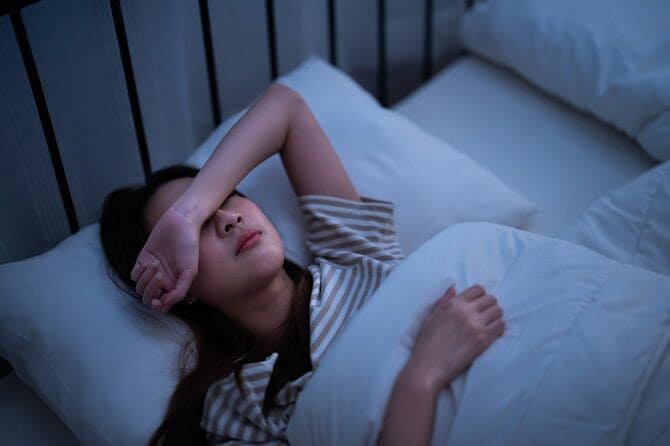 腕で目を覆いながら眠ろうとしている不眠の女性