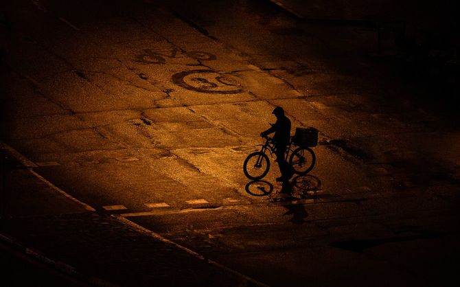 雨の降るなか、スマホを確認しながら自転車を押すウーバー配達員