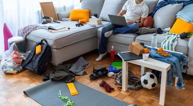 乱雑に散らかった部屋でノートパソコンを使用してる男性