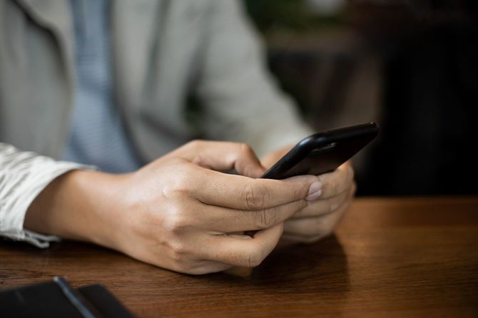 テーブルの上で携帯電話を握り、入力するビジネスマン