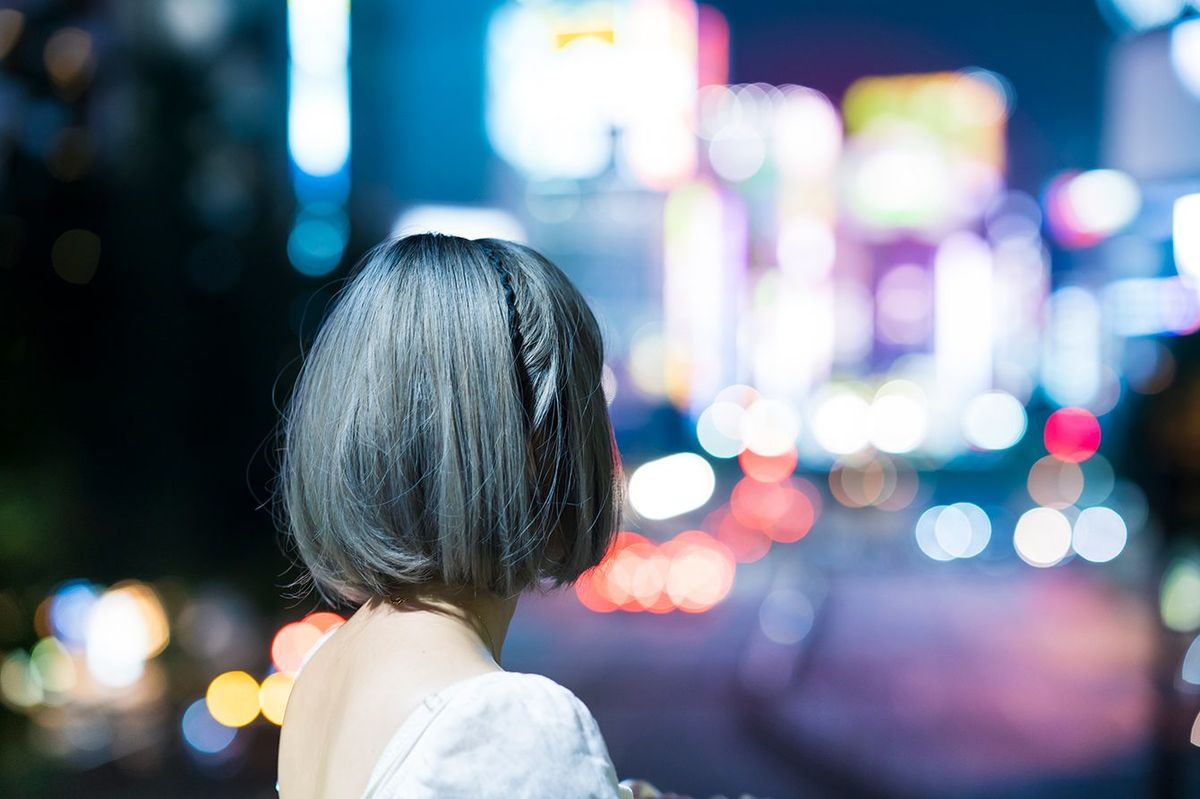 夜の東京の輝く街並みでポーズをとる若い女性