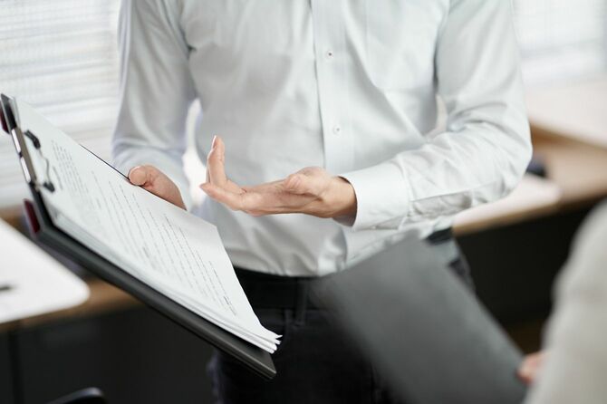 バインダーに挟んだ書類を示しながら説明する人の手元