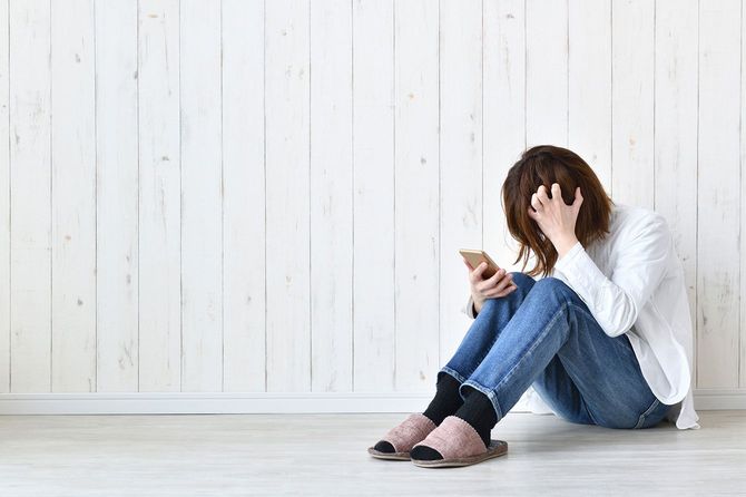 床に座り込んで頭を抱えてスマホを見ている女性