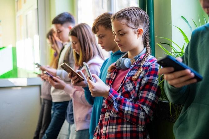 教室の窓側に一列に並んだ子供たちが皆スマホに目を落としている