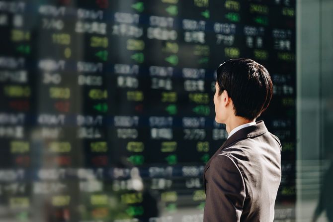 オフィス街に設置された屋外電光掲示板の株価掲示板を見るビジネスパーソン