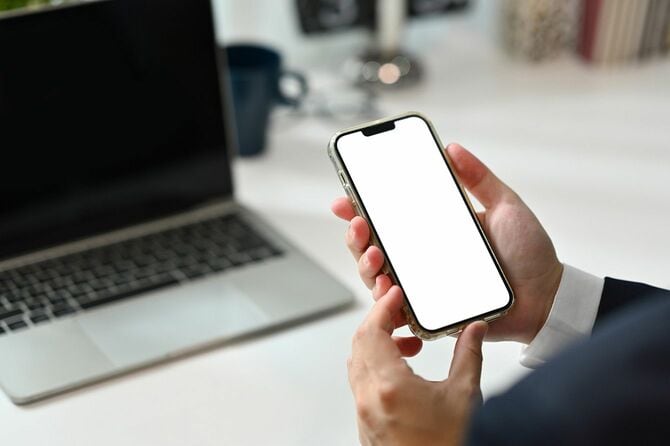 職場のパソコンの前でスマートフォンを持つ男性