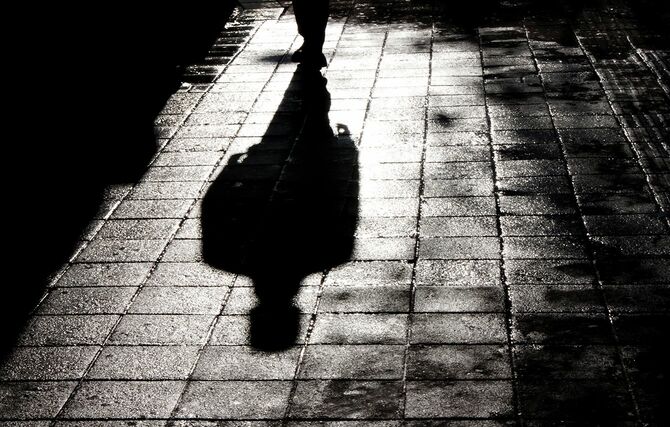 黒と白の水の反射で濡れた街の通りの歩道で夜に立っている男のぼやけた影とシルエット