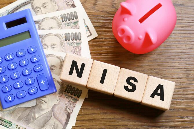 NISAと書かれた木製キューブと一万円札、電卓、豚の貯金箱