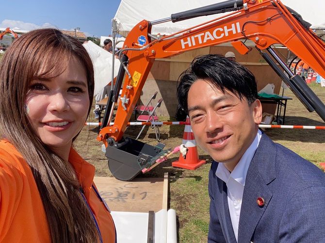 3年前の『よこすか建設フェスタ』で披露した重機習字。画面中央のユンボに乗っている女性が東さん、その右側にいるのが小泉進次郎農林水産大臣(当時)。ユンボを操作して「建設」の「建」を書いた