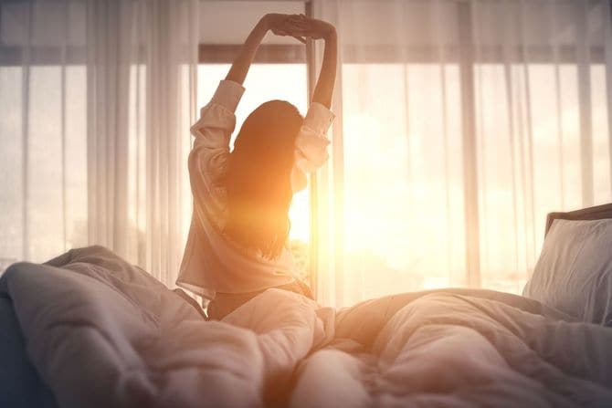 目を覚ました後、ベッドで伸びる幸せな女性