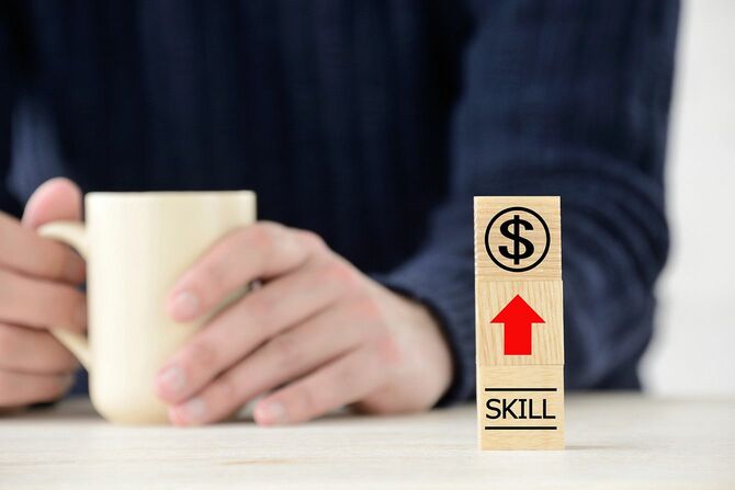 スキルアップしてお金を稼ぐという意味のアイコンを前にして、コーヒーカップを手にする男性