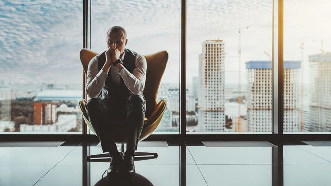 高級オフィスビルの窓の前の肘掛け椅子に座り、考え込む男性