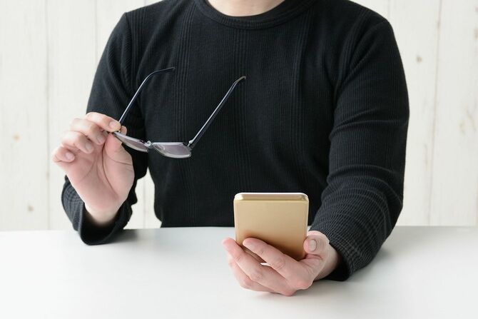 眼鏡をはずしてスマホを見る男性