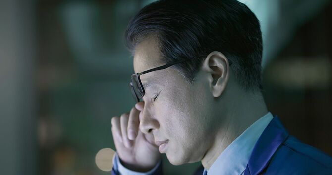 目をこする中年のビジネスパーソン