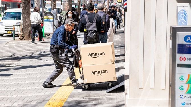 台車を押す高齢の配達員、新宿の街頭歩道でアマゾンの箱の荷物を届ける