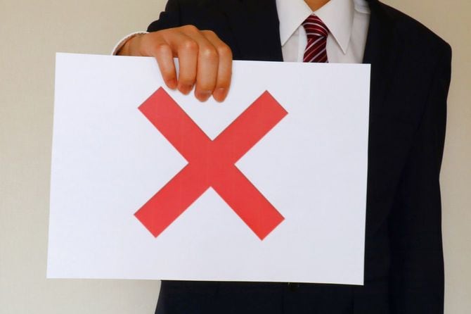 バツ印の書かれた紙を持っているビジネスマン