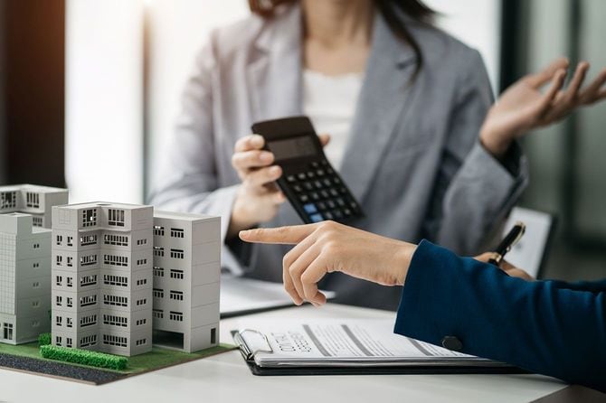 マンションの模型を前に、電卓で計算した金額を見せる不動産会社の担当者