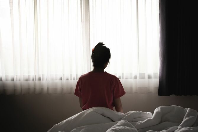 うつ病のアジアの女性は、朝ベッドに座って悲しいと孤独な感じを持っています