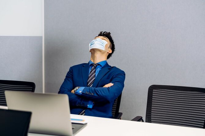 オフィスでマスクをして目を閉じるビジネスマン