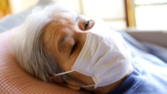 ウイルス保護のためにサージカルマスクを着用して横になるシニア女性