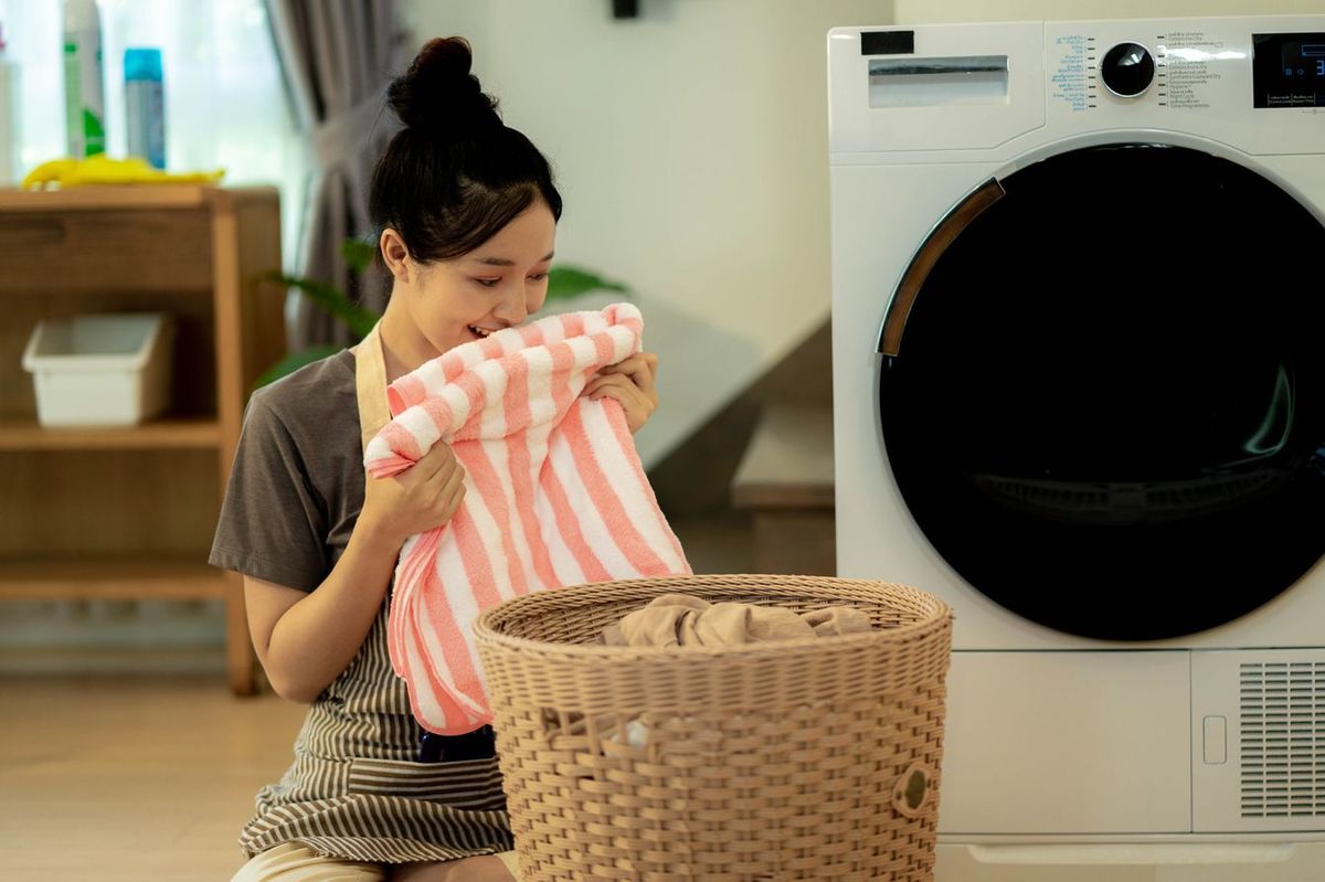 ドラム式洗濯機の前でタオルのにおいをかぐ女性