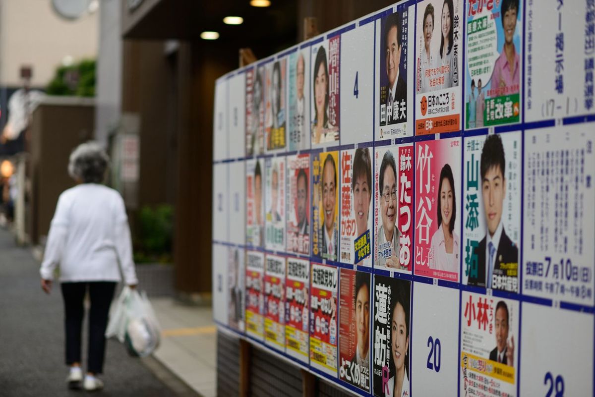 2016年の参議院選挙のポスター掲示板の前を通り過ぎるシニア女性