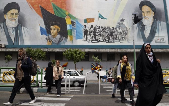 2024年4月16日、イラン・テヘランで、イラン最高指導者ハメネイ師(上左)とイラン最高指導者故ルーホッラー・ホメイニー師(上右)の壁画の前を歩くイラン人たち