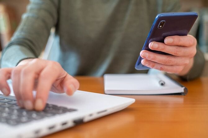 スマートフォンを持ってラップトップコンピューターで作業する人