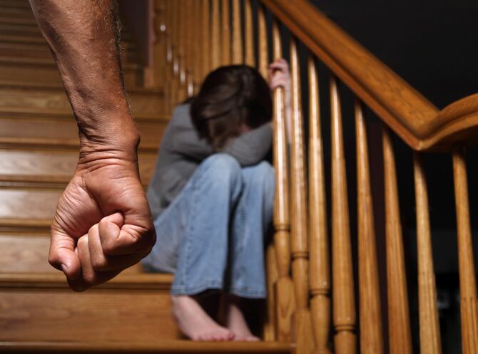 児童虐待のイメージ。階段にうずくまって泣いている子と成人男性の握りこぶし