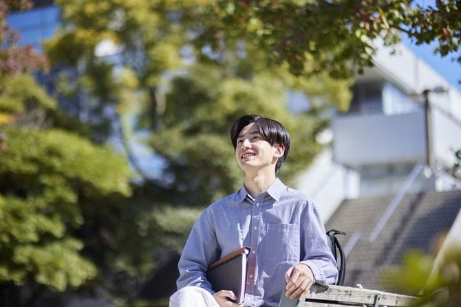 大学のキャンパスのベンチに腰かけている男子学生