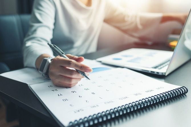 ラップトップで作業をしながらカレンダーを書き込む女性