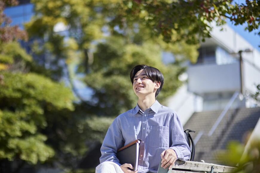 大学のキャンパスのベンチに腰かけている男子学生