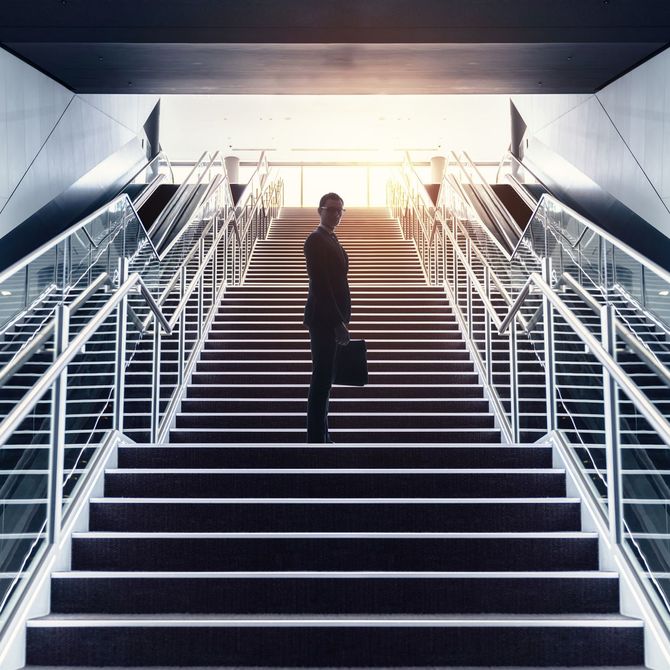 長い階段の途中でこちらを振り向く逆光のビジネスマン