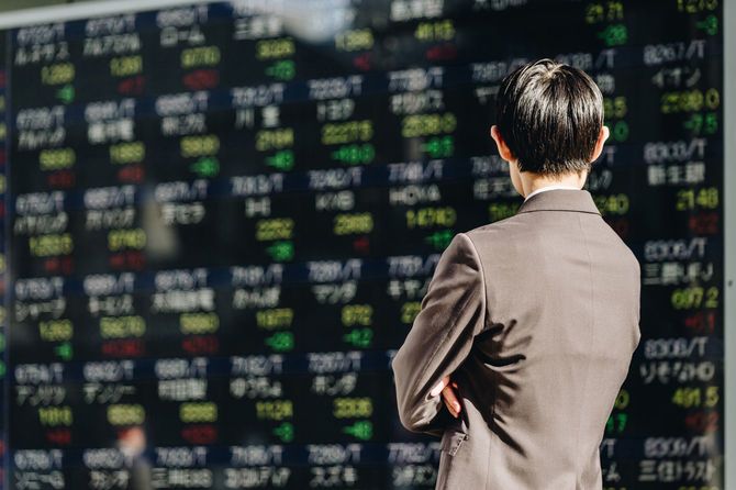 電光掲示板に表示された多数の銘柄の株価を見る男性