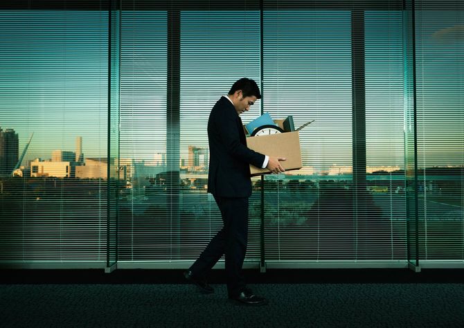 段ボール箱を持ってオフィスを移動するうつむいたサラリーマン