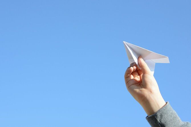 青空背景に子供の手と紙飛行機