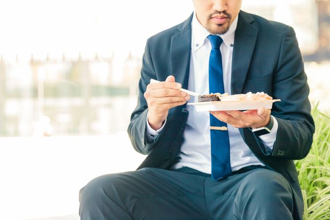 外で弁当を食べる若いサラリーマン