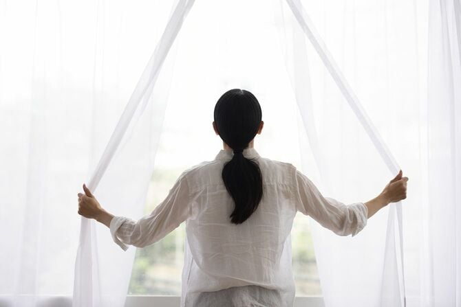 朝の光を入れるためにカーテンを開ける女性
