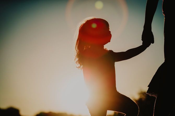 夕日に照らされて、母の手を握る少女のシルエット