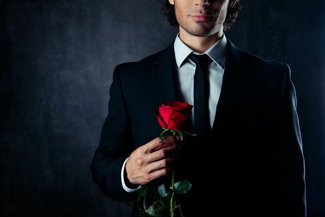 赤のバラを保持しているハンサムな若い彼氏のクローズ アップ