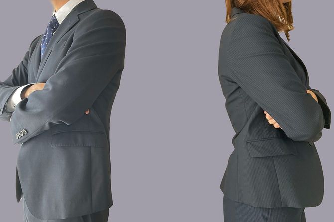 互いに背を向けて腕組みをして立っている2人のビジネスパーソン