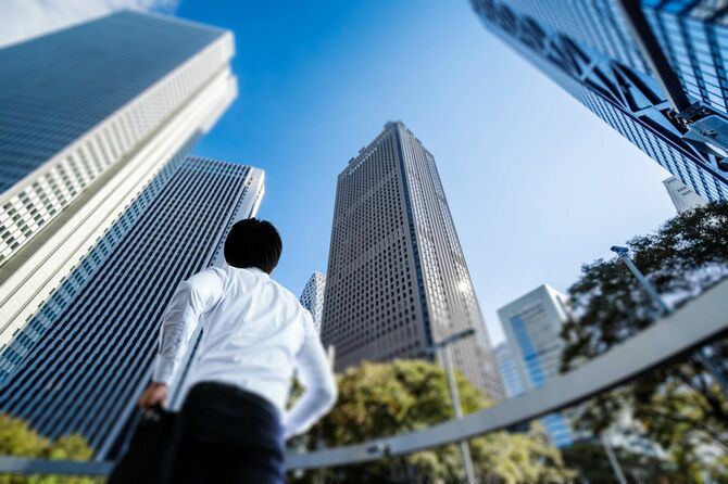 高層ビルの立ち並ぶオフィス街で見上げる男性