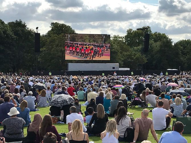 大型画面に映し出される棺が運ばれる様子を見守る人々