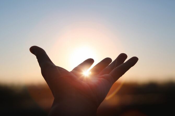 新年の日の出の昇る太陽に向かって手を伸ばし、指の間を照らすまばゆい光