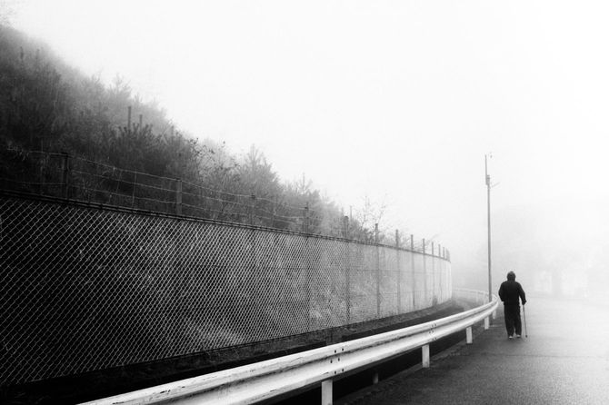 霧の中、杖をついて歩いているシニア男性の後ろ姿